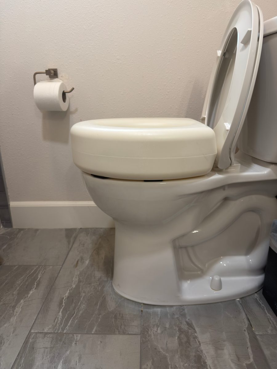 The white plastic raised toilet seat riser I used, on a round toilet bowl, seen from the side